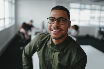Fototapeta premium Portrait of charming successful young african american entrepreneur in shirt and eyeglasses looking at camera with smile in office