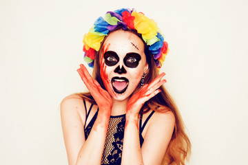 Halloween party, girl in costume and with halloween make-up. A girl in blood, with scars and with a make-up skeleton. A girl with flowers on her head looks at the camera.
