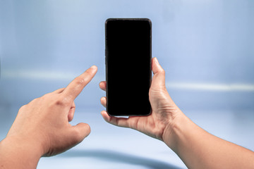 Hand holding Modern mobile smart phone with black screen for mockup on Blue background . Close-up of hands sliding using smartphone are shopping and searching or Selfie on social networks concept  .