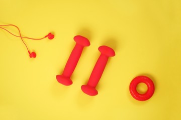 Top view of dumbbell, headphones, carpal expander, apple on a yellow background with space for text. Creative flat lay sport and fitness concept.