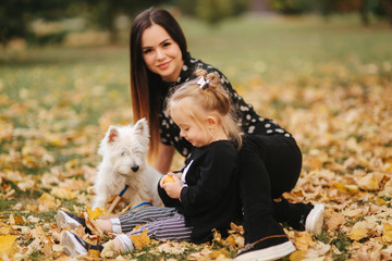 Happy mother and her daughter playing with dog in autumn park. Family, pet, domestic animal and lifestyle concept. Autumn time.