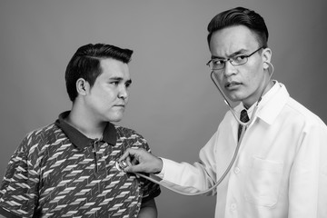 Young multi-ethnic man and young Indian man doctor against gray background