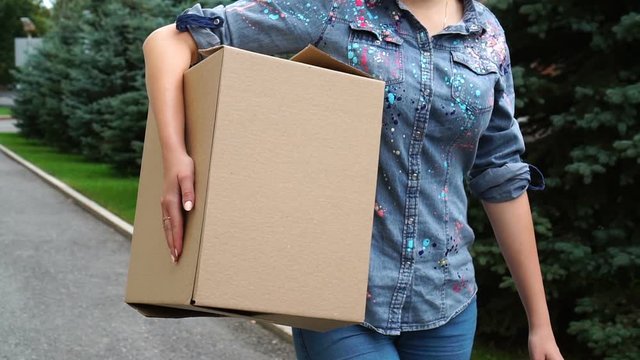 Unrecognizable woman carrying a cardboard box and walking outdoor