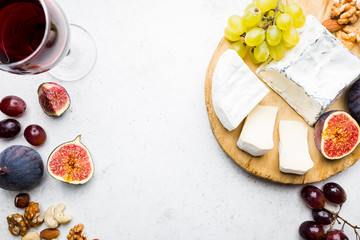 Camembert or brie cheese with fresh figs, honeycomb and glass of wine on serving board over white...