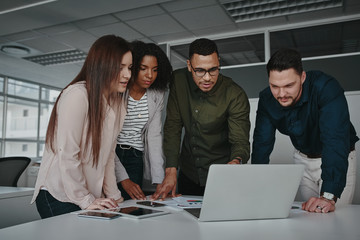Group of smart young multiethnic businesspeople discussing ideas while looking at laptop computer