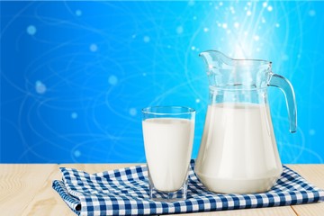 Glass of milk and jar on table with cloth and background
