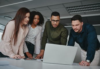 Group of concentrated diverse business team discussing information on laptop screen over the desk in office