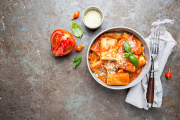Pasta paccheri with tomato sauce and basil in a plate, top view