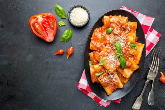 Pasta paccheri with tomato sauce and basil in a plate, top view