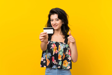 Young woman over isolated yellow background holding a credit card