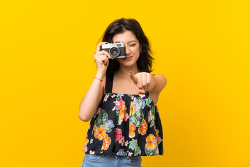 Young woman over isolated yellow background holding a camera