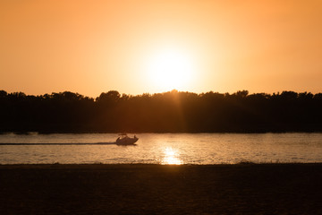 A yacht cruising along the river with a male sitting at the front of it, enjoying the picturesque sunset.