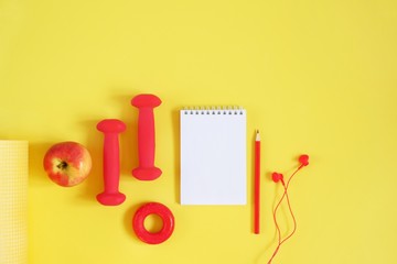 Creative flat lay sport and fitness concept. Top view of dumbbells, headphones, hand expander, apple, notebook and pencil on a yellow background with space for text.