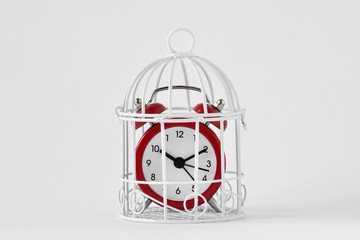 Red alarm clock in a cage on white background - Concept of time limit - obrazy, fototapety, plakaty