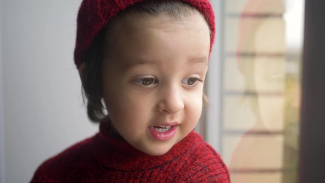 boy child in a red sweater and a knitted hat sits on a large white window