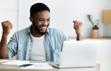 Euphoric black man celebrating business success with raised arms