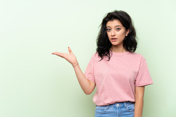 Young woman over isolated green background making doubts gesture