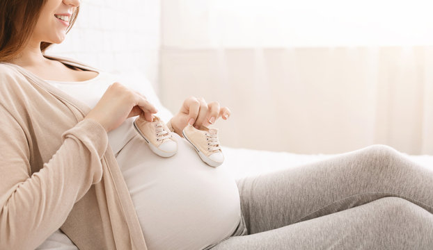 Pregnant woman playing with tiny shoes, stepping on belly