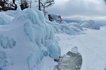 Lake Baikal in the winter. Crystal clear ice covers the lake. Coastal stones and rocks are covered with a layer of ice.