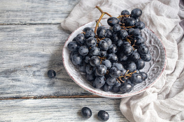 Large, black, wine grapes. It is covered with a white coating called yeast. With the help of them, wine is obtained. Drops of water on the berries, next to a gray fabric for decoration. 