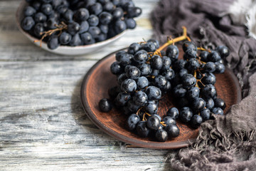 Large, black, wine grapes. It is covered with a white coating called yeast. With the help of them, wine is obtained. Drops of water on the berries, next to a gray fabric for decoration. 