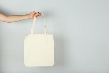 Female hand holding white cotton eco bag on grey background