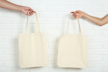 Female hands holding cotton eco bags on white brick wall background