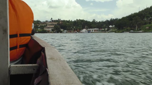 Boat sails towards land during a boat trip on lake Kivu. At the background landscape with buildings and a little harbour