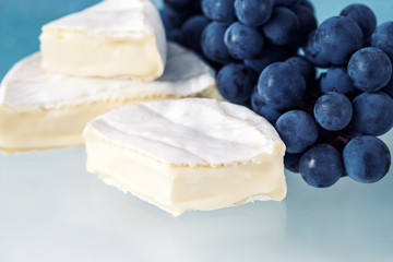 White Camembert cheese, melted cheese with mold, cheese and grapes on a light blue background
