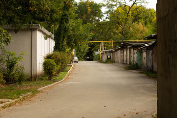 Cozy street with alley of garages and green trees, autumn weather
