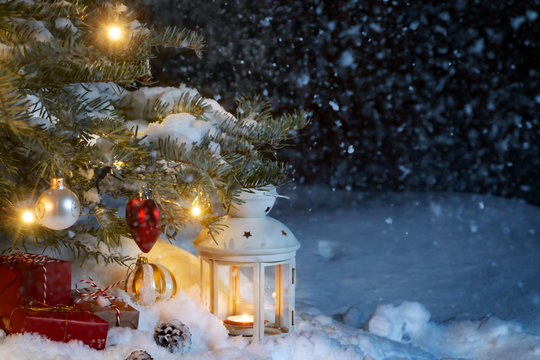 Christmas composition - gifts and a lantern in the snow under a Christmas tree decorated with lights and Christmas-tree decorations, copy space, place for text