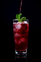 Process of pouring the red drink into a tall glass filled with ice cubes, raspberries and mint...