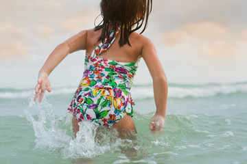 A little girl in a bathing suit playing in the waves at the beach