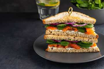 Sandwiches with cream cheese, salmon and spinach on a dark background.