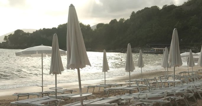 Umbrellas and beach beds in Lerici, near the Cinque Terre. Sunlight at sunset with sea waves and trees in the background.