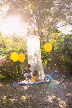 Two little girls playing outside and reading books in the yard in a shade tent with balloons