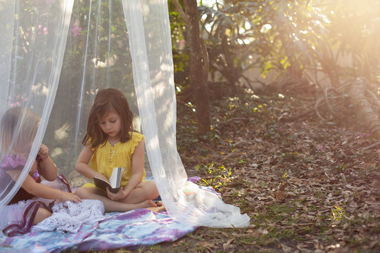 Two little girls playing outside in the yard in a shade tent with balloons