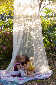 Two little girls playing outside and reading books in the yard in a shade tent with balloons