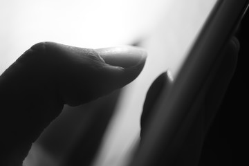 Human finger typing on a gadget screen. Black and white macro photo.