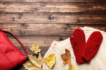 Woolen sweater with gloves, red bag and autumn leafs on brown wooden table