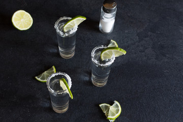 Shot glasses of gold tequila with a rim of salt, and lime slices.