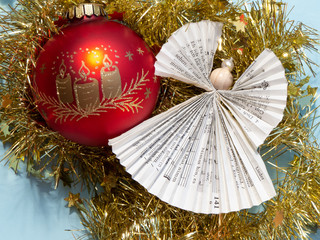Christmas angel made out of sheet of music and red Christmas ball ornament on golden tinsel in...