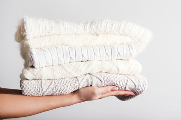 Female hands holding folded knitted sweaters on grey background