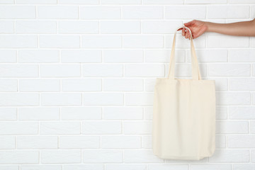 Female hand holding cotton eco bag on white brick wall background