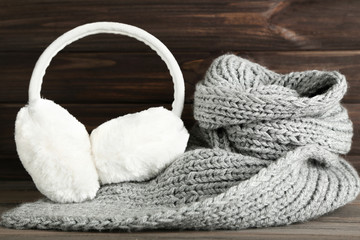 Knitted scarf with fluffy earmuffs on wooden background