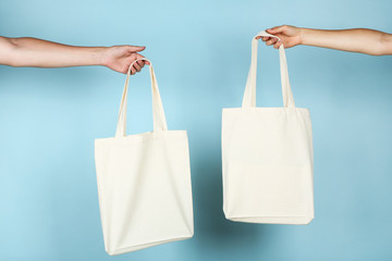 Female hands holding white cotton eco bags on blue background