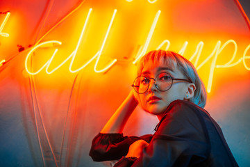 Young adult asian female wearing glasses in front of neon light sign, shallow selective focus