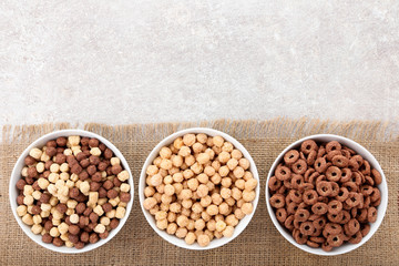 Various corn flakes in bowls on grey background