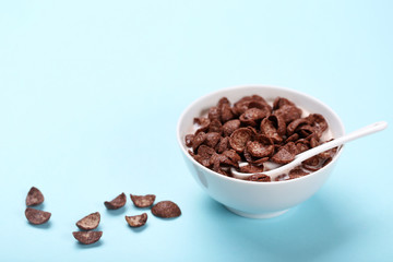 Chocolate corn flakes in bowl with milk and spoon on pink background