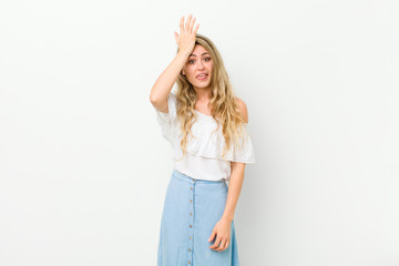 young blonde woman raising palm to forehead thinking oops, after making a stupid mistake or...
